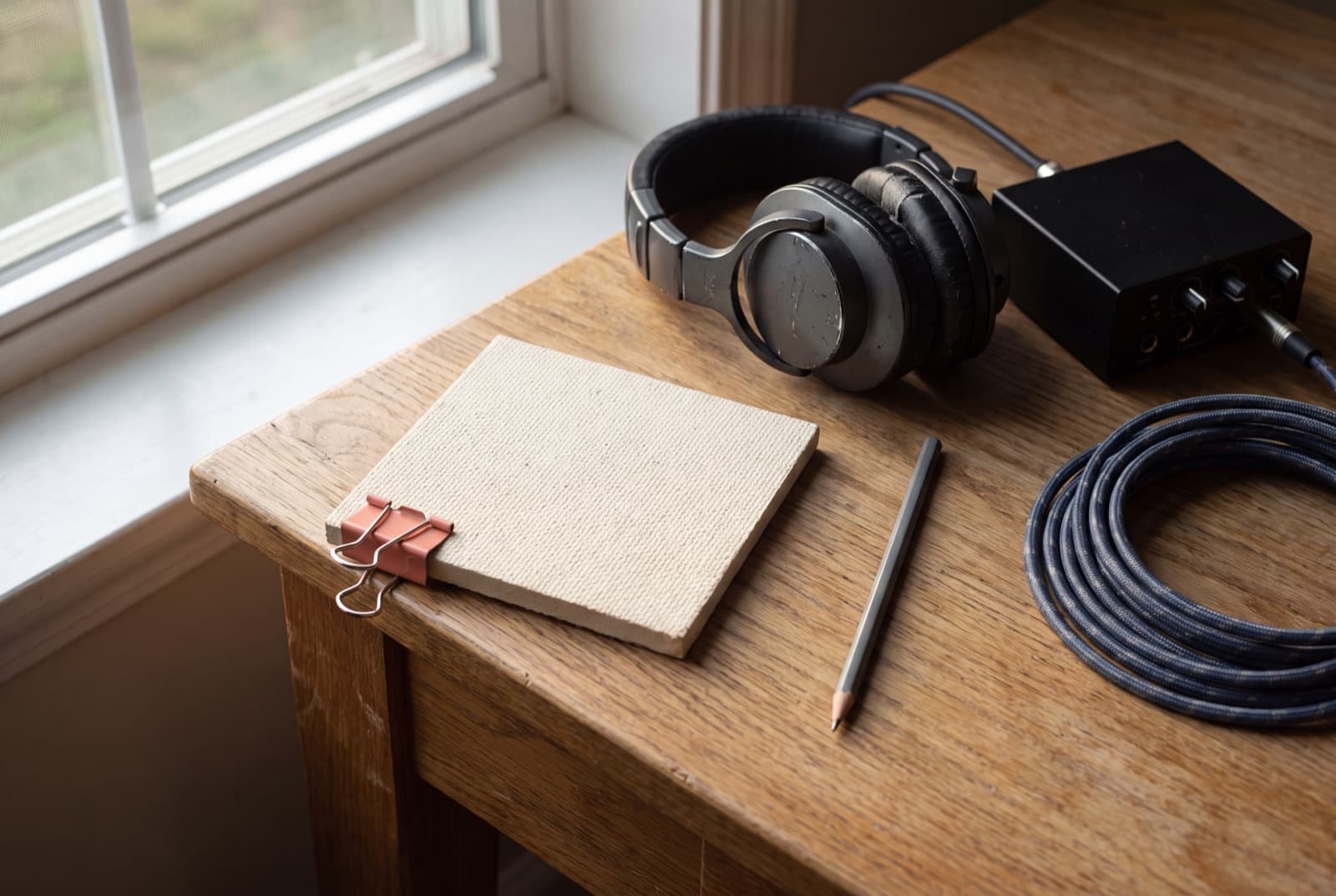 Studio headphones and a blank acoustic tile beside a compact audio controller on a warm table