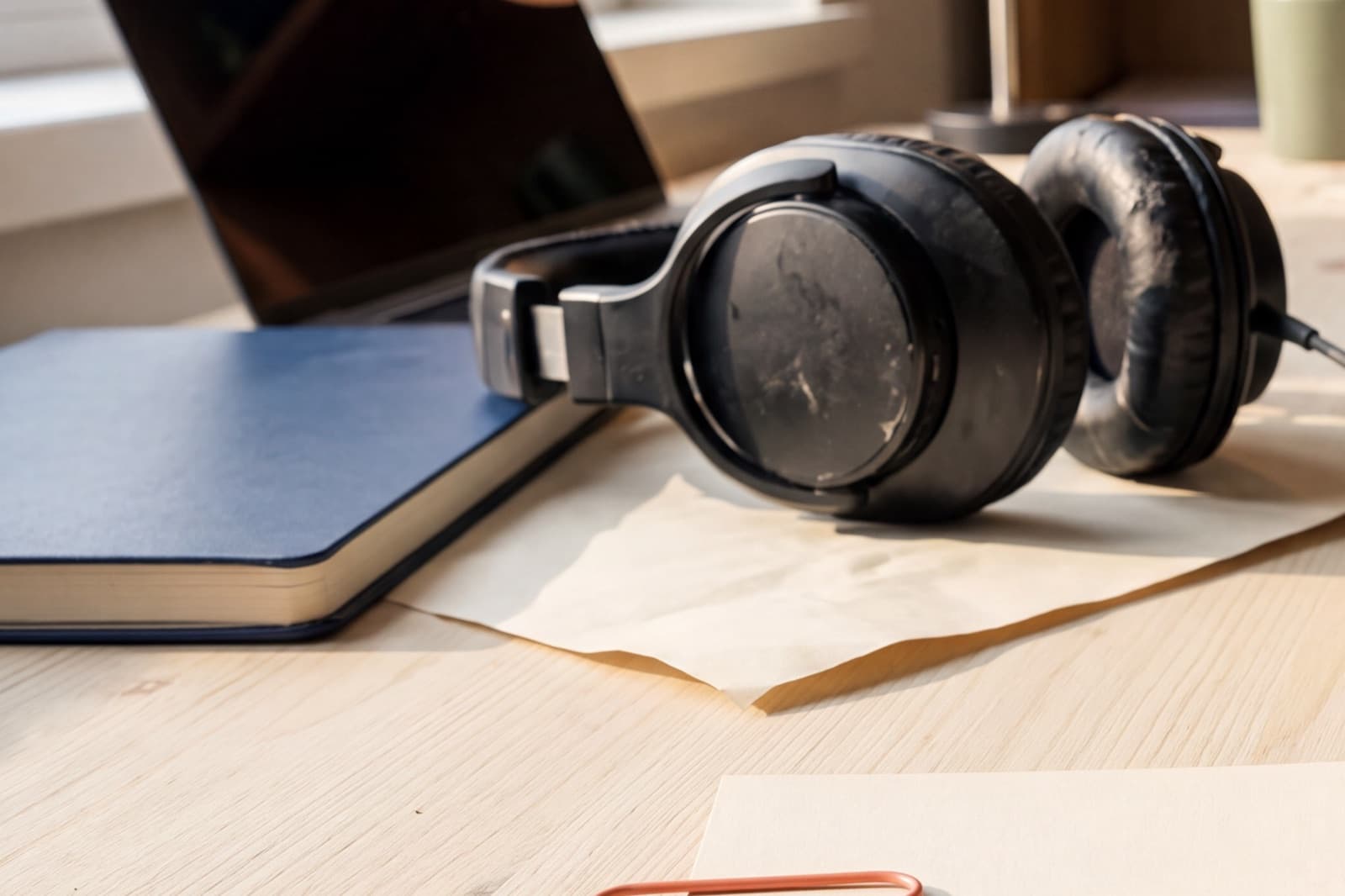 Studio headphones beside a blank review packet and coral paper clip at the final approval handoff